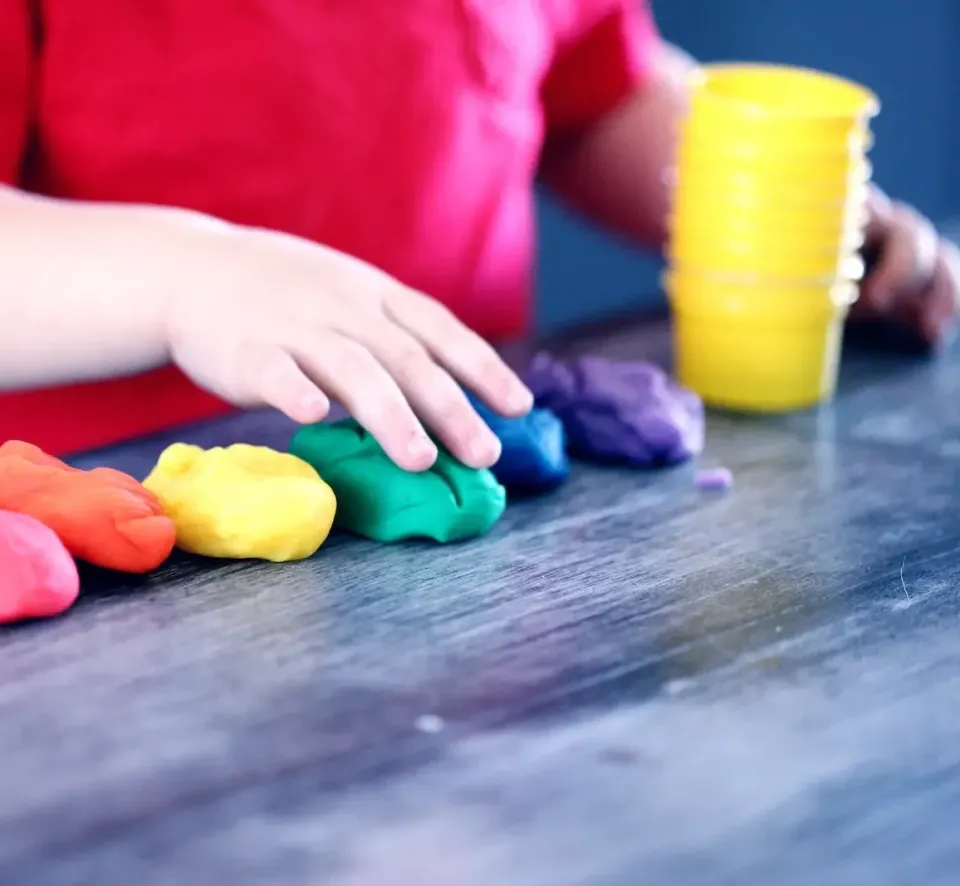Kinderhände formen bunte Knete am Tisch